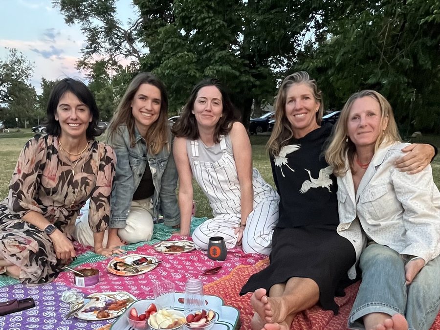 Five friends sitting together on a picnic blanket in a park at dusk.