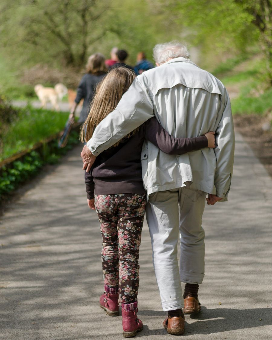 A grandfather and a child walking hand in hand along a garden path.