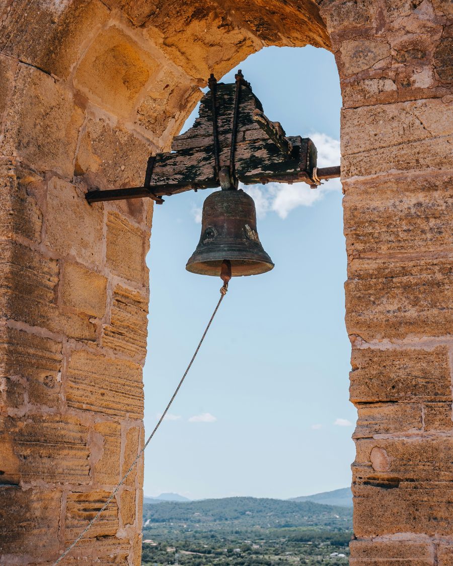 An old bronze bell hanging in a stone arch against a blue sky