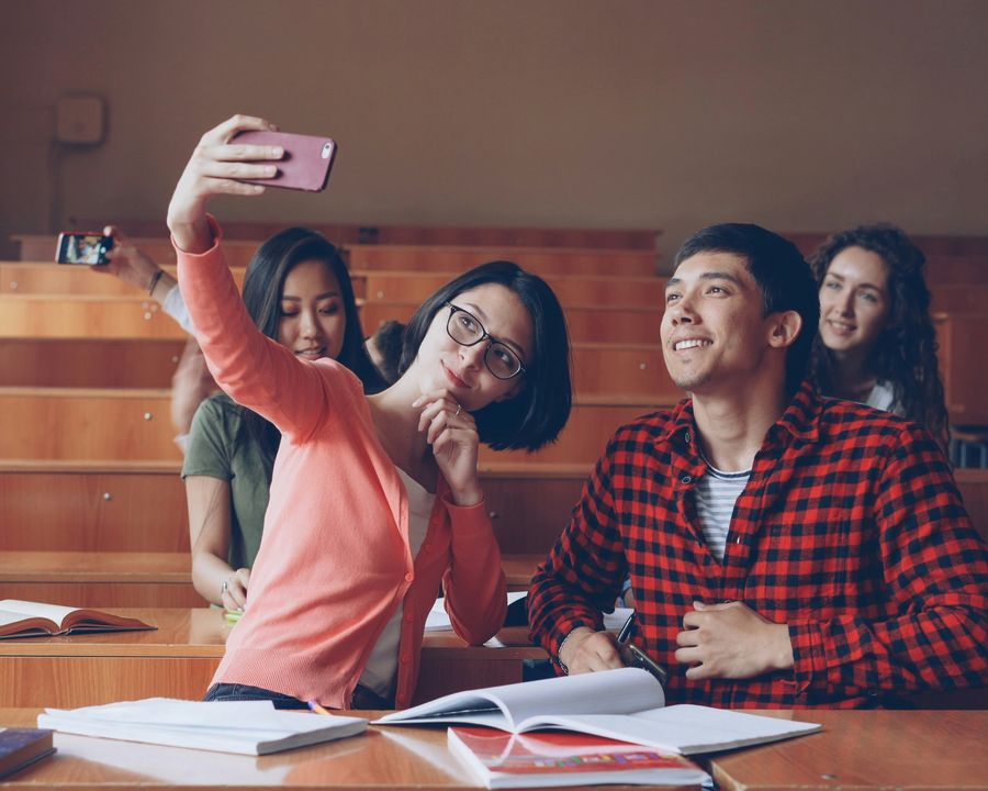 Four students in a lecture hall, leaning in for a group selfie.