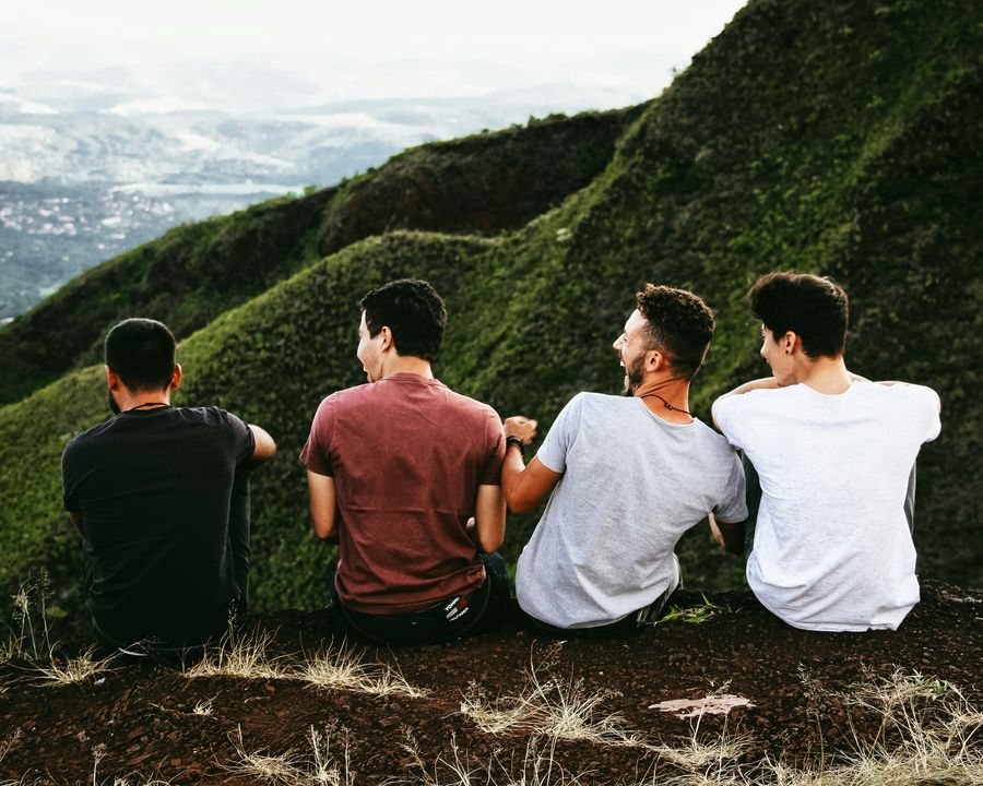 Four friends sitting on a grassy hillside, looking out over the valley together.