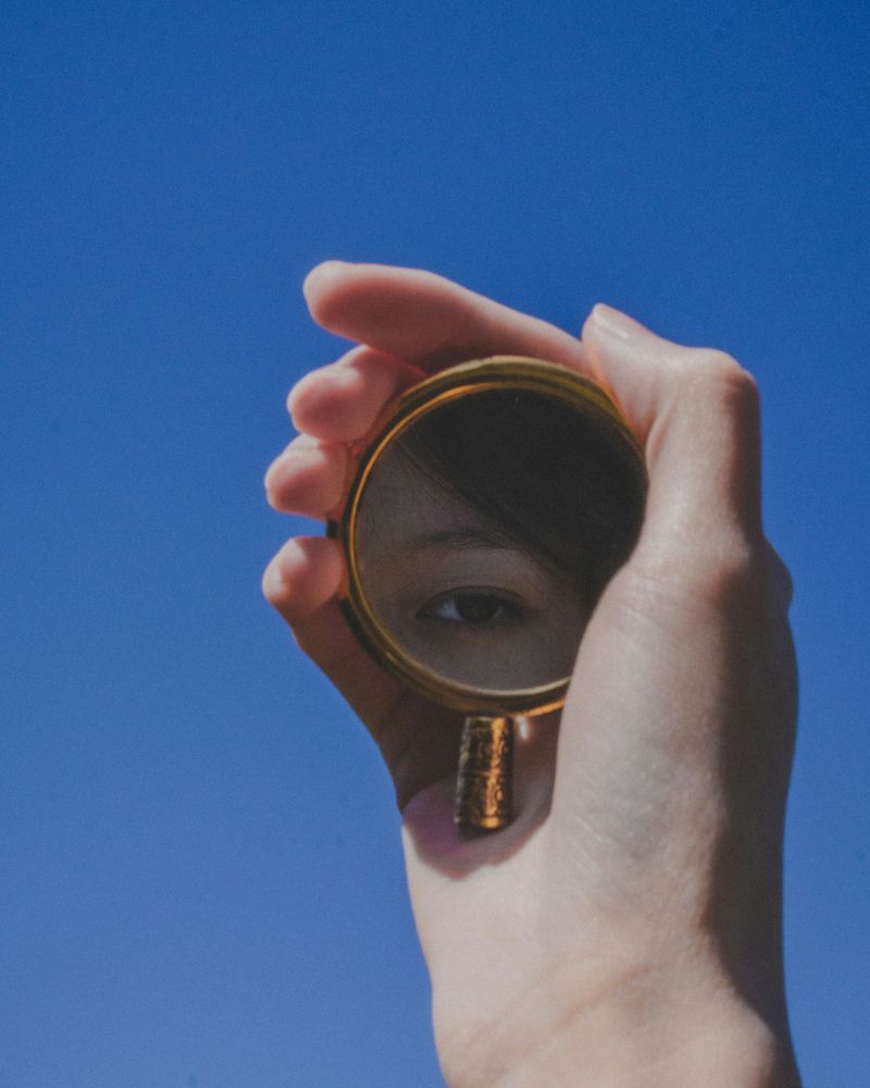 A hand holding a small round mirror reflecting an eye