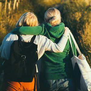 Two friends walking arm in arm in evening light.