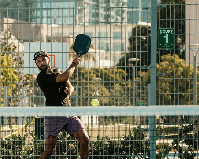 A man mid-swing on an outdoor pickleball court.