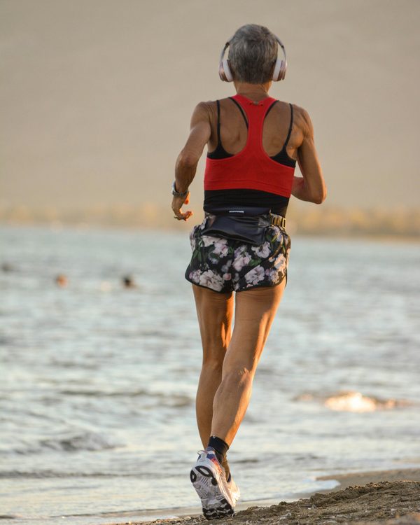An older woman running along the shoreline at sunrise.