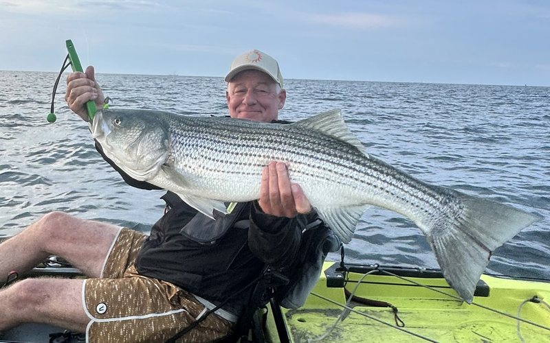 An older man in a kayak holding up a large fish
