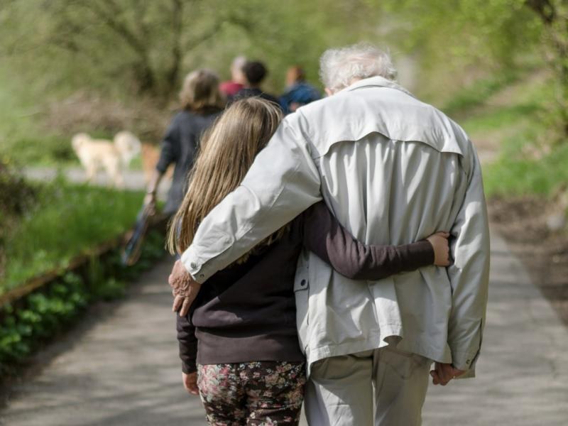 An older man and a child walking arm in arm down a garden path