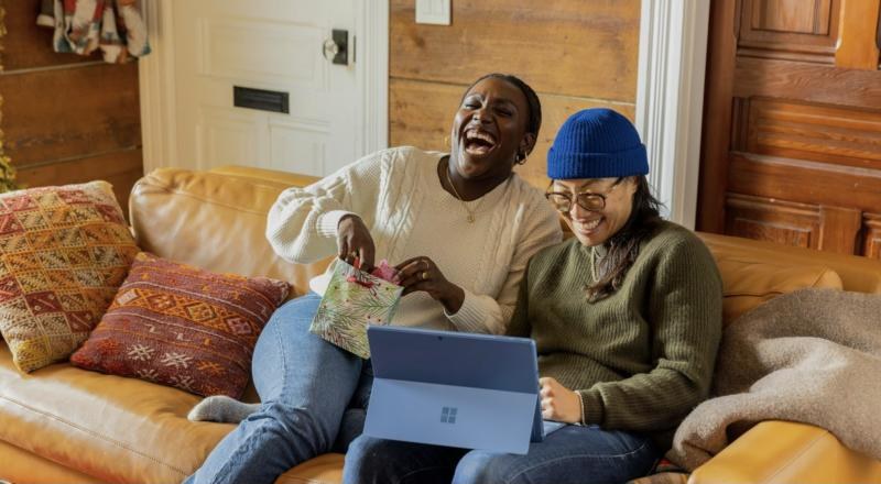 A woman laughing on a couch with a laptop